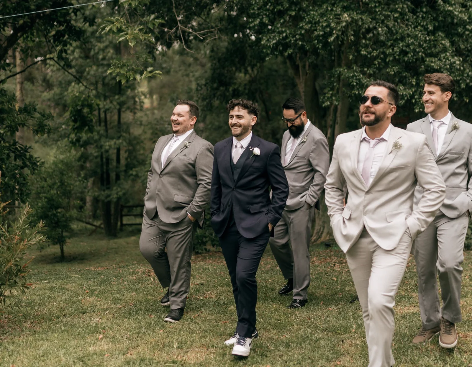 Illustrative wedding party walking together in coordinating suits outdoors.
